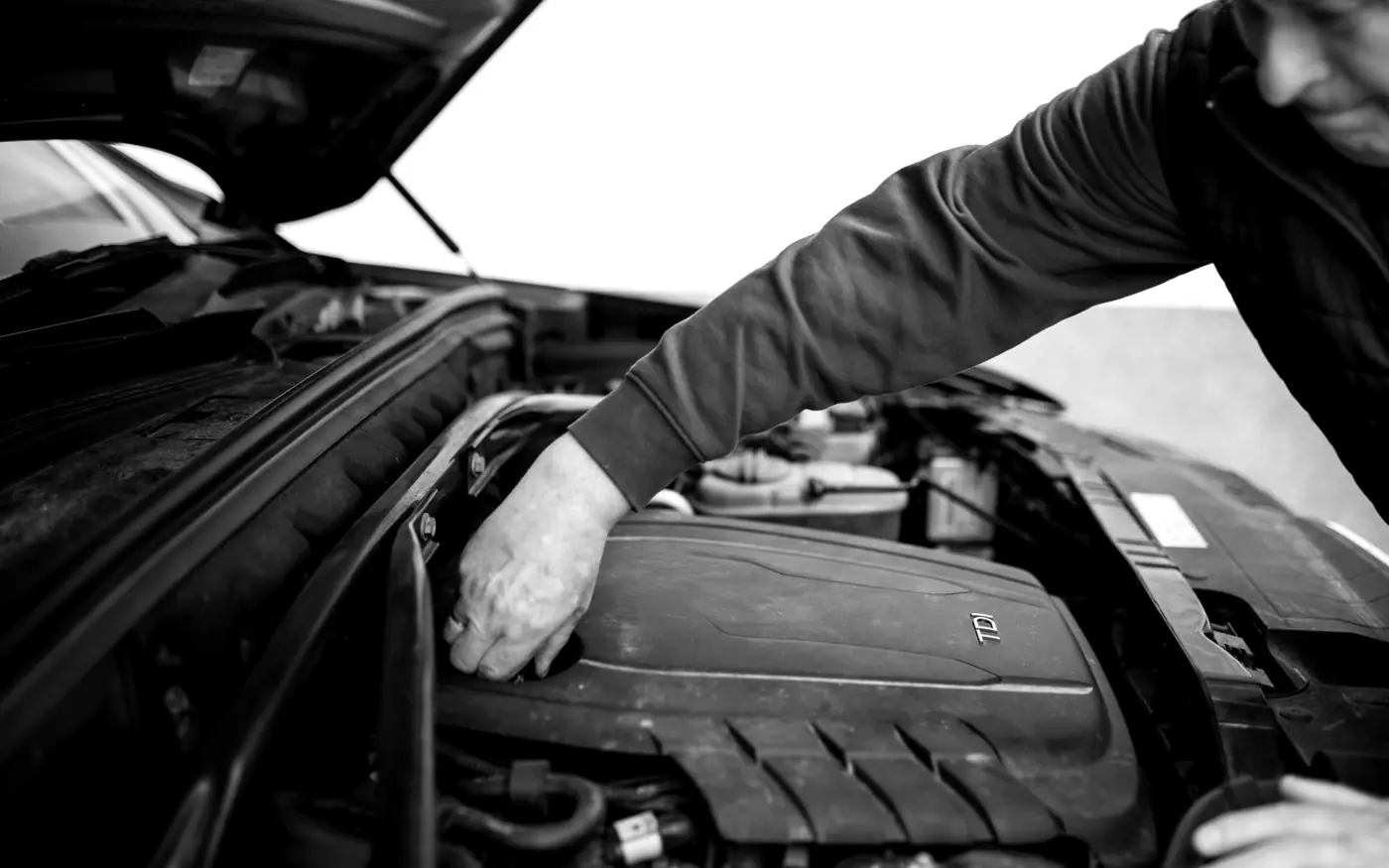 Handen van een monteur aan het werk in een geopende motorruimte.